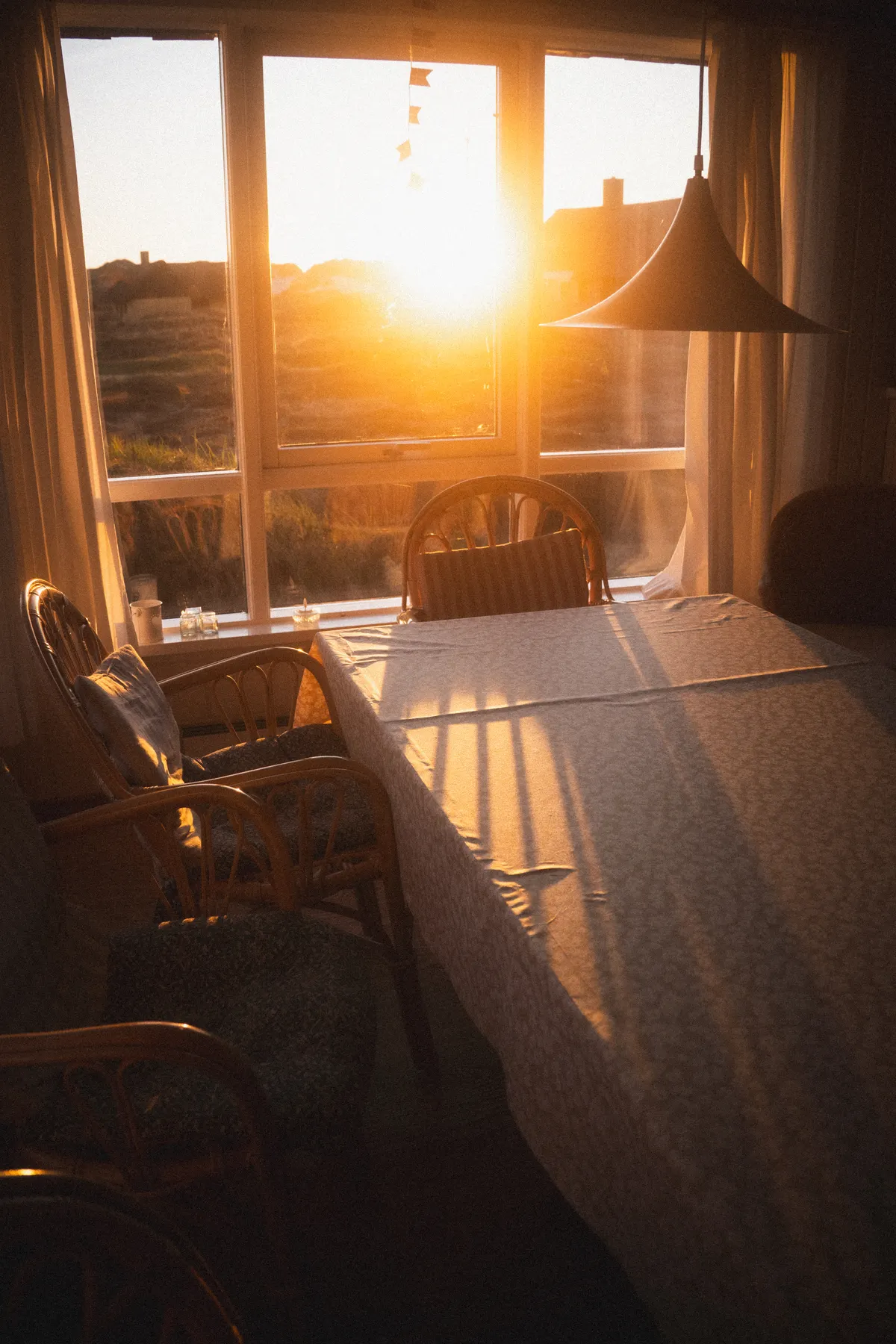 Late sunlight crosses a white-clothed dining table beside a broad window.