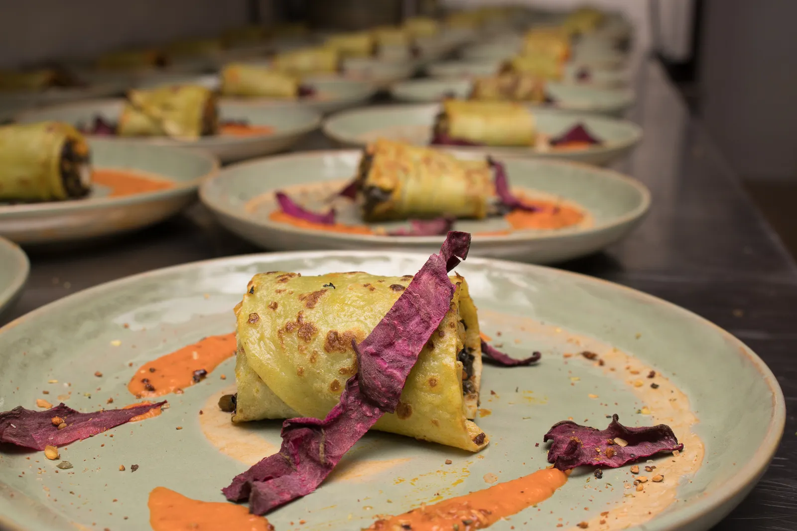 A line of pale ceramic plates holds rolled seasonal courses ready for service.