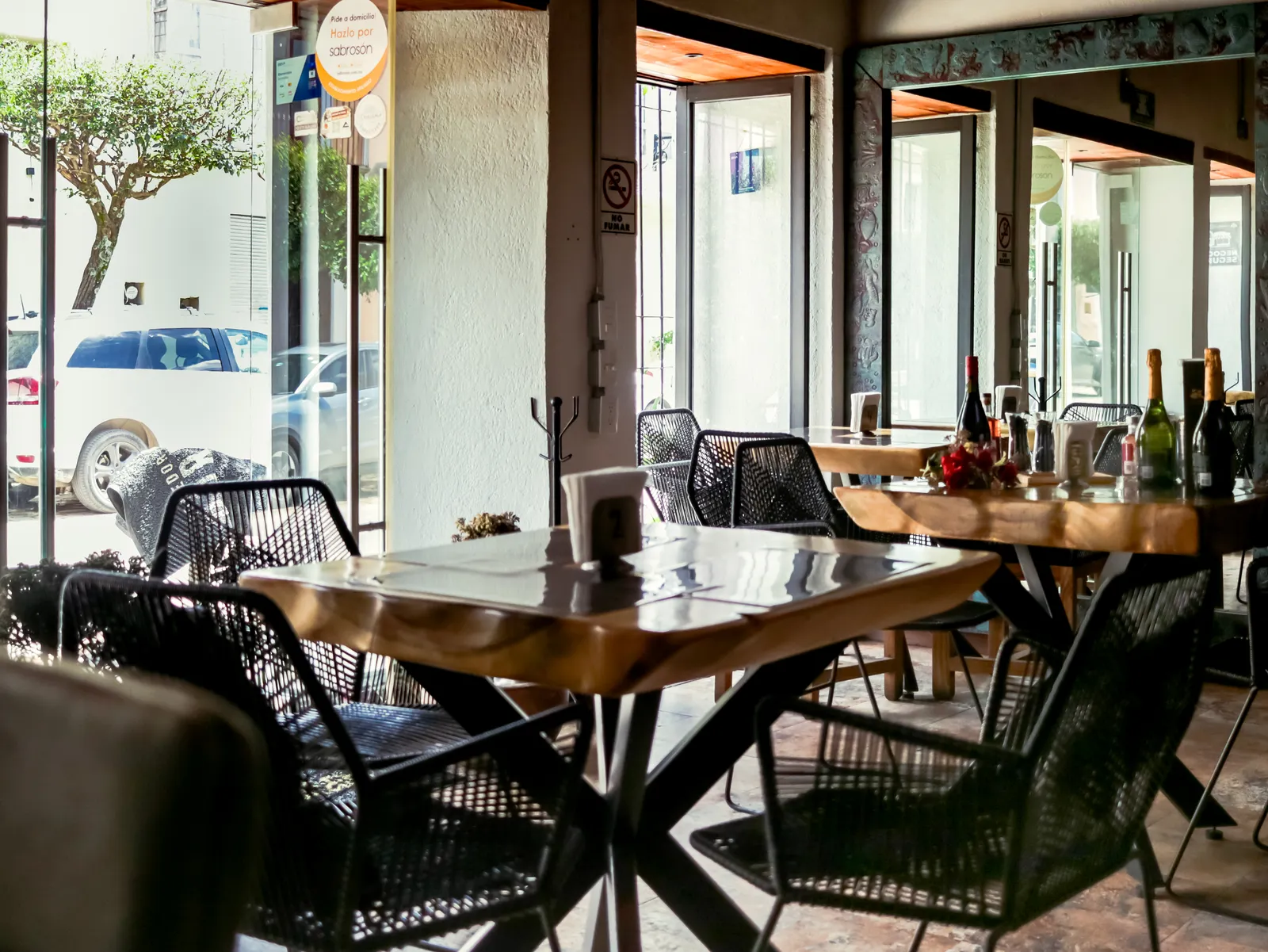 Natural light reaches wooden tables and dark woven chairs in an empty dining room.